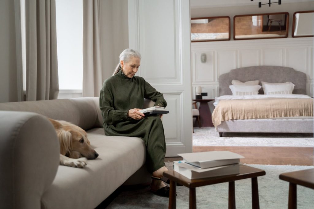 Elderly Woman Reading Book at Home with Dog - best apartment dogs for seniors